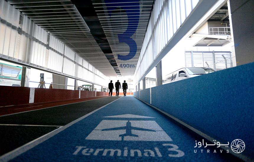 تصویری از «ترمینال شماره 3» فرودگاه که از زاویه کف آبی‌رنگ ترمینال ثبت شده و سه مردِ یونیفرم‌پوش را در انتهای تصویر نشان می‌دهد.